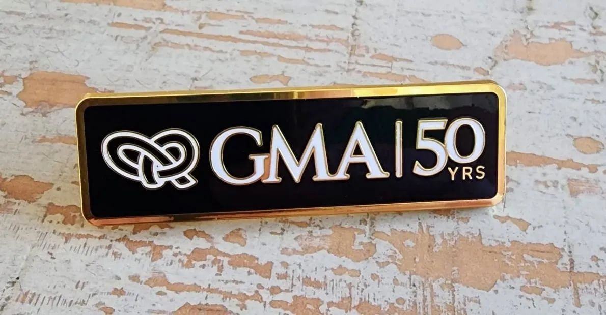 The GMA 50 Years pin: the Infinite Links knot and GMA | 50 YRS in white on black enamel, edged in gold